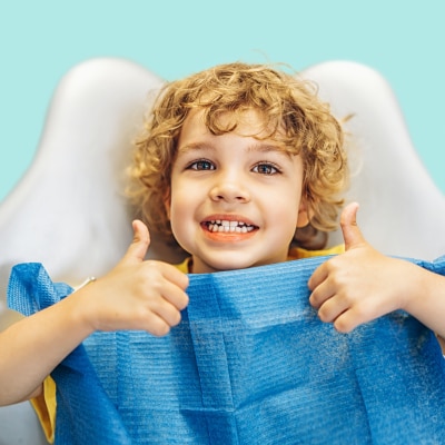 Boy in dentists chair giving two thumbs up